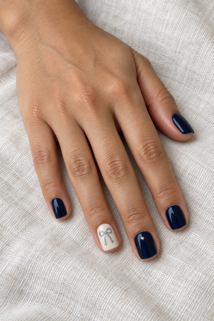 Short navy nails with an ivory accent, silver ribbon bow and small silver dot.